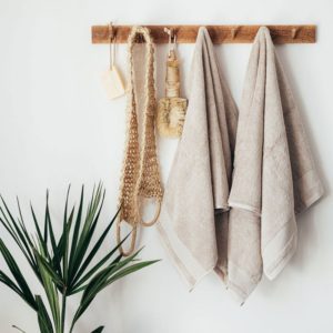 Image of high quality bamboo towels hanging hooks beside a decorative plant. 
